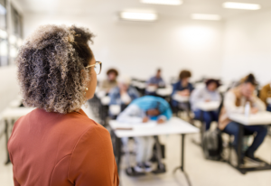 Professor acompanha estudantes dos anos iniciais em atividade de leitura, representando o desafio da alfabetização na idade certa nas redes municipais.